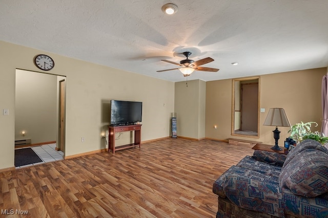 unfurnished living room featuring a baseboard heating unit, baseboards, a textured ceiling, and light wood finished floors