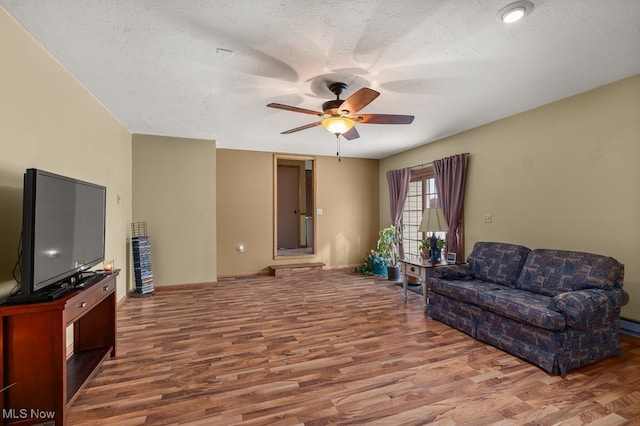 living area featuring a textured ceiling, wood finished floors, a ceiling fan, and baseboards