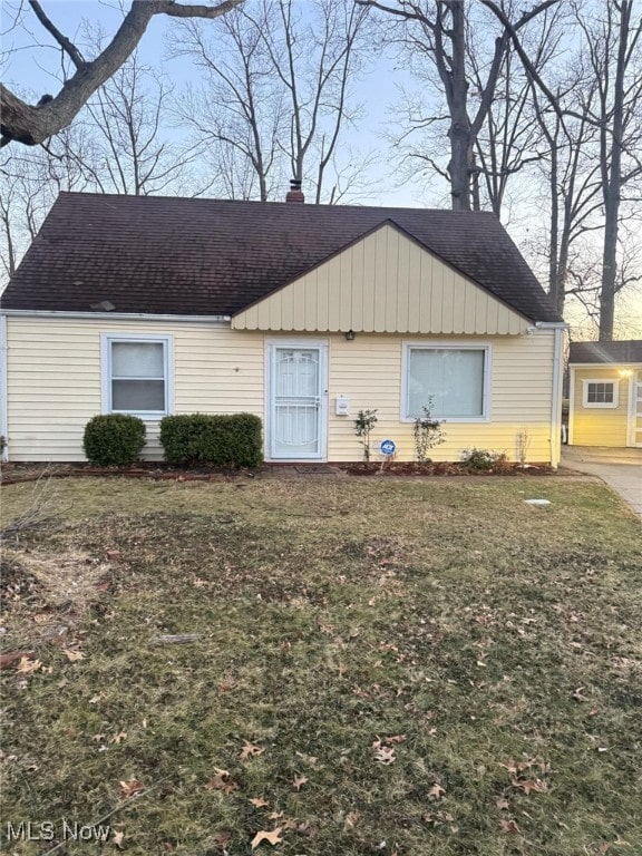 view of front facade featuring a front lawn, a chimney, and a shingled roof