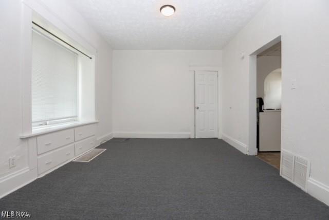 spare room with arched walkways, dark colored carpet, visible vents, and baseboards