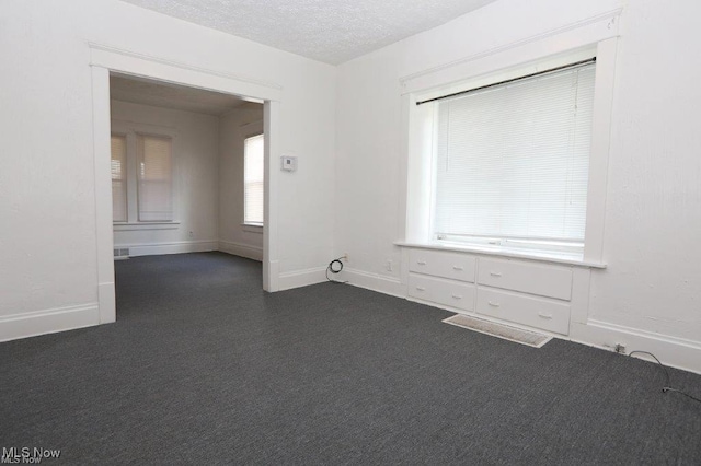 spare room featuring a textured ceiling, dark carpet, and baseboards