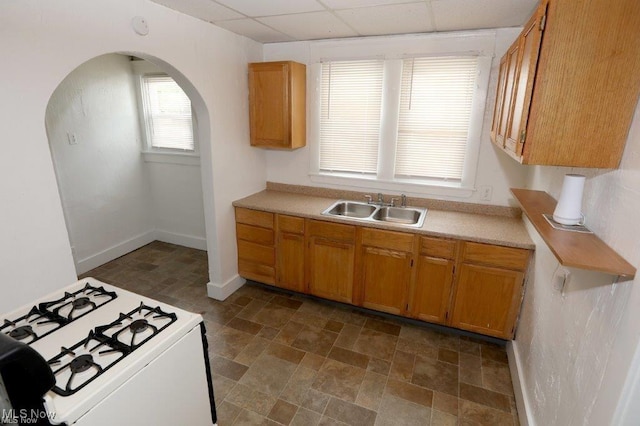 kitchen featuring gas range gas stove, arched walkways, light countertops, and a sink