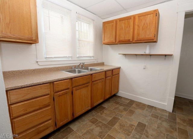 kitchen with baseboards, stone finish floor, light countertops, a paneled ceiling, and a sink