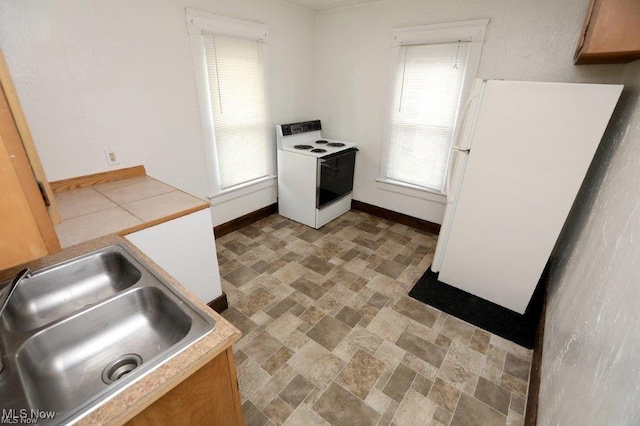 kitchen featuring light countertops, white appliances, a sink, and baseboards