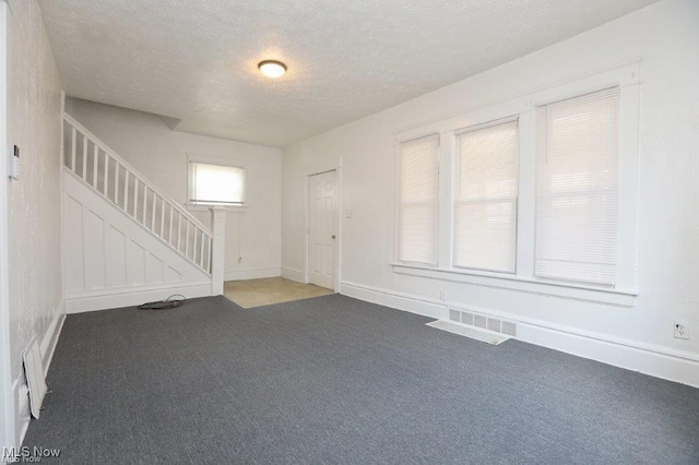 carpeted foyer with a textured ceiling, stairway, visible vents, and baseboards