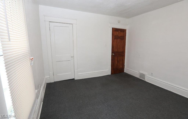 unfurnished room featuring visible vents, dark carpet, and baseboards