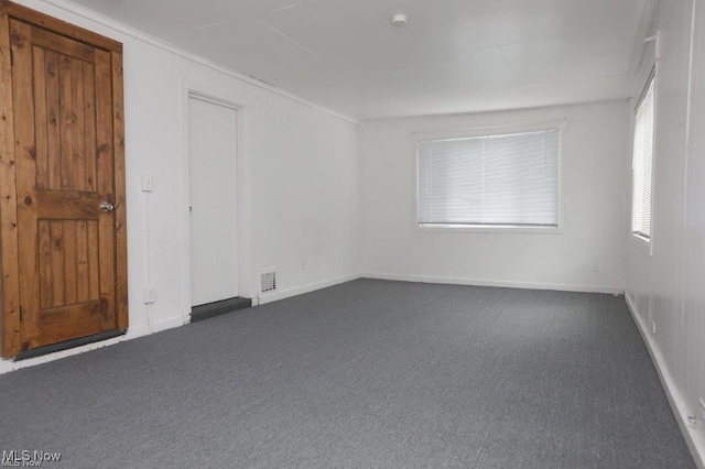 empty room featuring visible vents, dark carpet, and baseboards