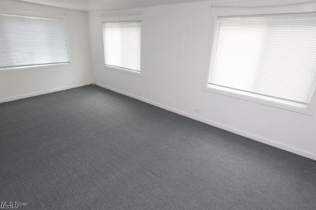 empty room featuring baseboards and dark colored carpet