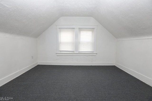 additional living space featuring a textured ceiling, dark carpet, and lofted ceiling