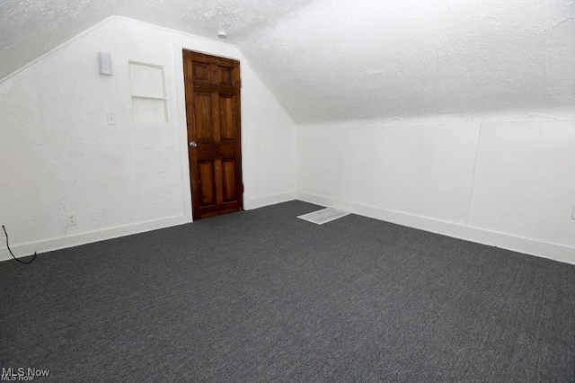 bonus room featuring baseboards, a textured wall, vaulted ceiling, dark colored carpet, and a textured ceiling