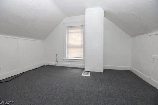 bonus room with lofted ceiling, a textured ceiling, visible vents, baseboards, and dark colored carpet