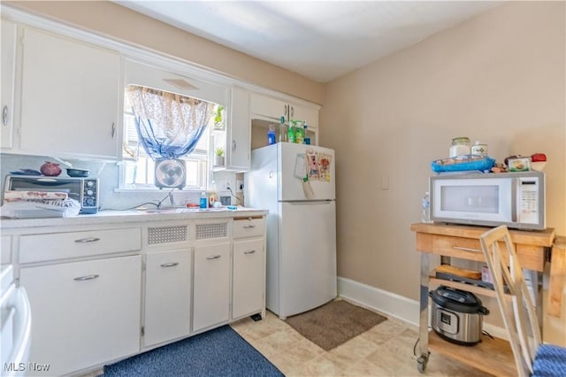 kitchen with white appliances, baseboards, white cabinets, light countertops, and a sink