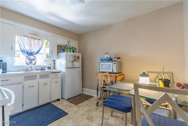 kitchen featuring white appliances, baseboards, white cabinets, light countertops, and a sink