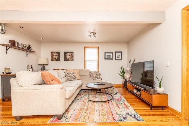 living area featuring beamed ceiling, light wood-style flooring, and baseboards