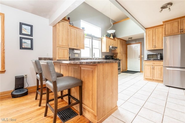 kitchen with a peninsula, stainless steel appliances, light brown cabinetry, under cabinet range hood, and a sink