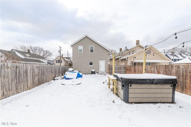 snow covered back of property with a fenced backyard and a hot tub