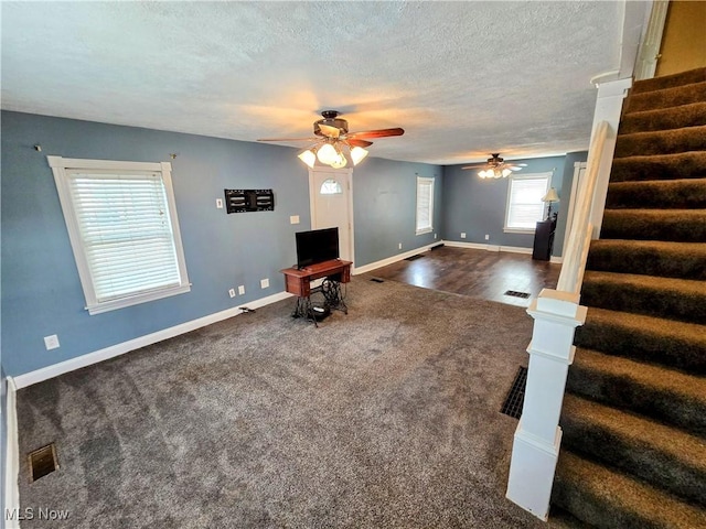 living area with a textured ceiling, visible vents, baseboards, stairway, and dark carpet