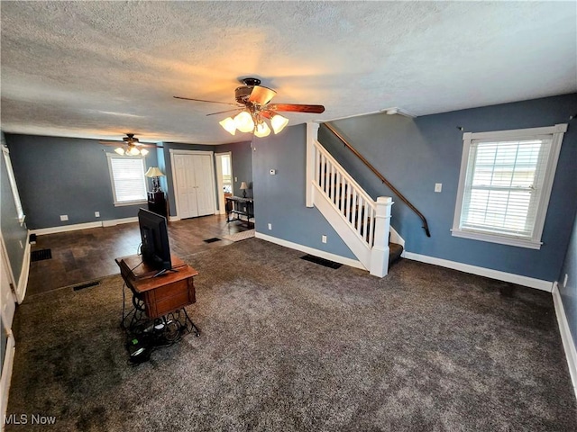 unfurnished living room featuring a textured ceiling, visible vents, baseboards, stairs, and dark carpet