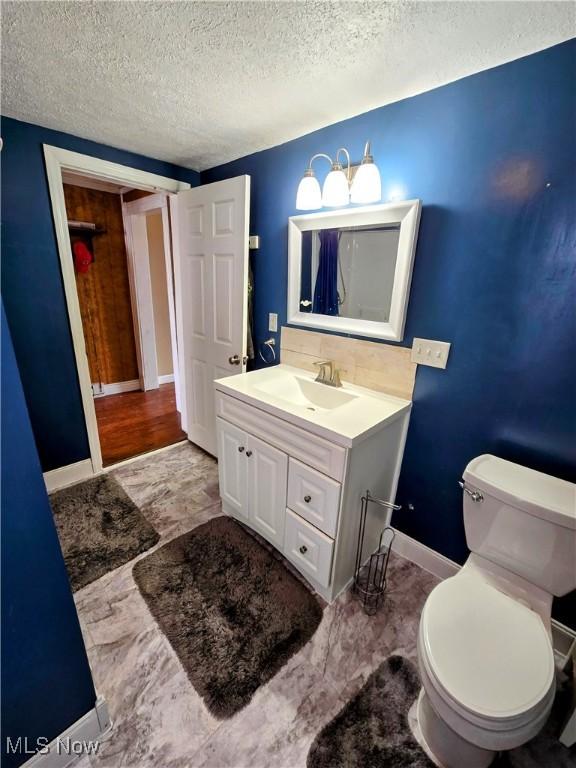 bathroom with toilet, baseboards, a textured ceiling, and vanity