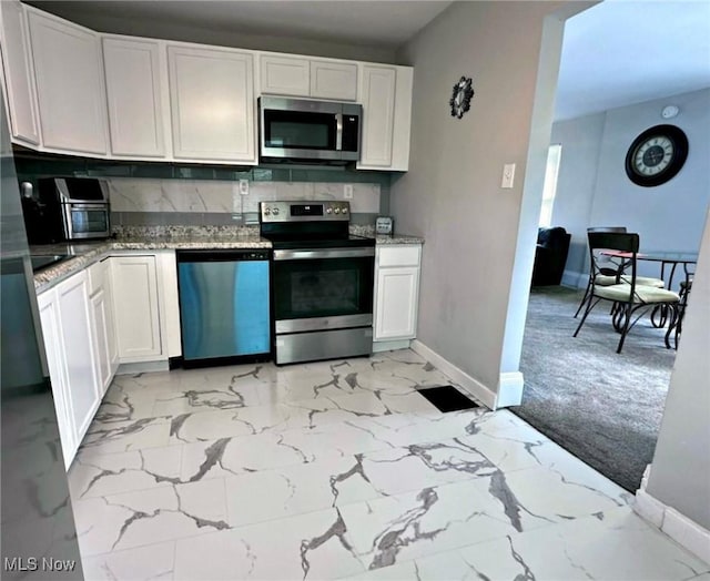 kitchen with marble finish floor, appliances with stainless steel finishes, light stone counters, and white cabinetry