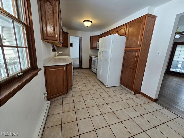 kitchen with a sink, white appliances, light countertops, light tile patterned floors, and a baseboard radiator