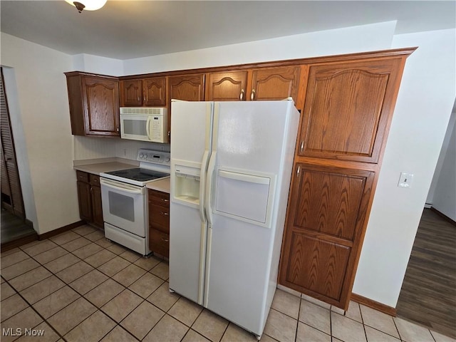 kitchen with light tile patterned floors, baseboards, white appliances, and light countertops