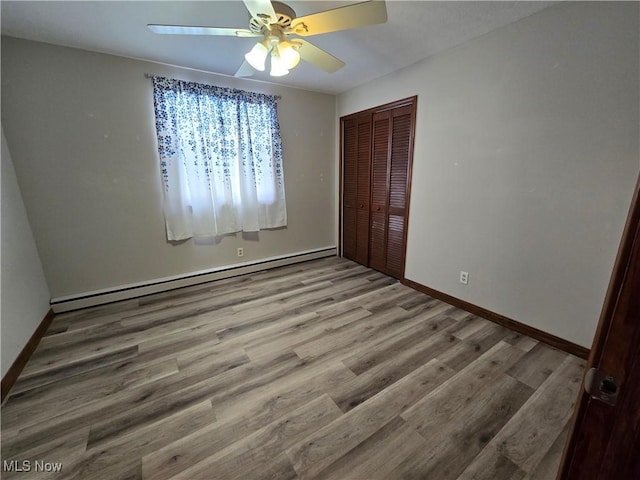 unfurnished bedroom featuring a closet, a baseboard heating unit, baseboards, and wood finished floors