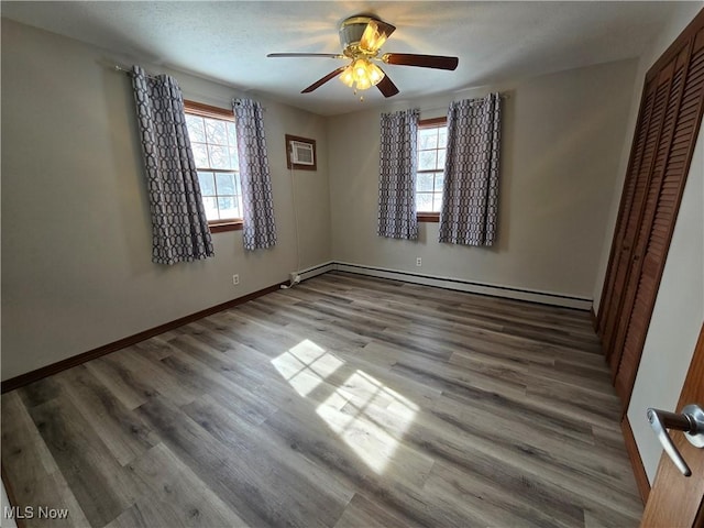 unfurnished bedroom with a baseboard heating unit, baseboards, a closet, and wood finished floors