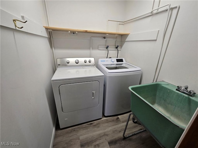 laundry area with laundry area, wood finished floors, washing machine and dryer, and a sink