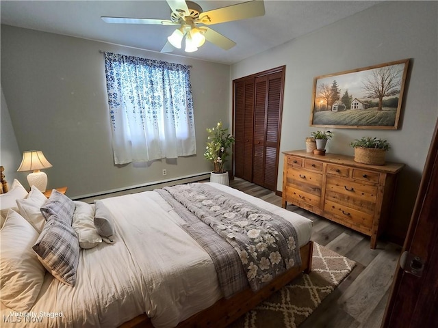 bedroom with a baseboard heating unit, wood finished floors, a closet, and ceiling fan