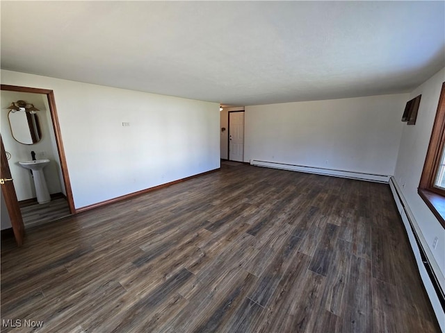 spare room with dark wood-style floors, baseboard heating, baseboards, and a sink