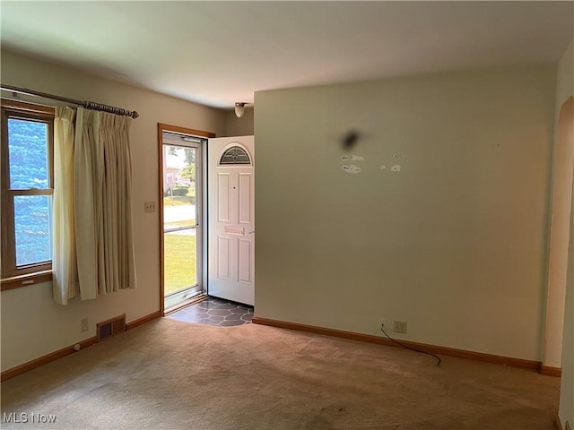 foyer with arched walkways, carpet flooring, visible vents, and baseboards