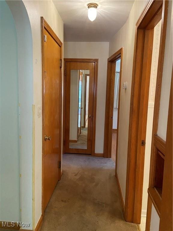 hall with arched walkways, light colored carpet, and baseboards