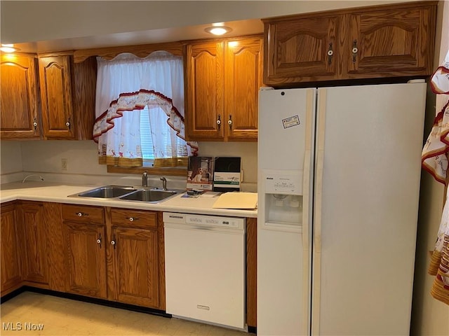 kitchen featuring light countertops, white appliances, brown cabinetry, and a sink