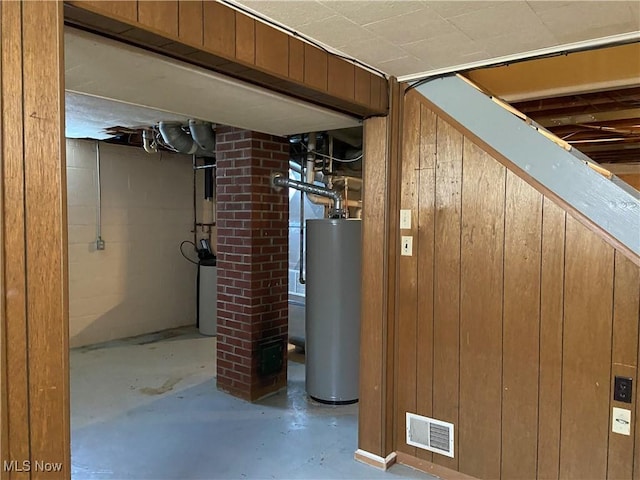 unfinished basement with gas water heater, visible vents, and wooden walls