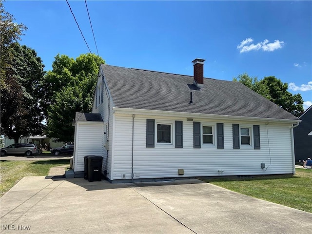 back of property with a yard, a patio, a shingled roof, and a chimney