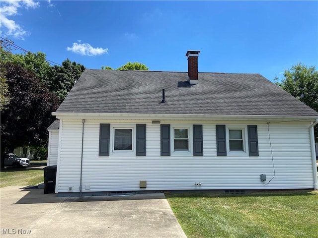 back of property featuring roof with shingles, a lawn, and a chimney