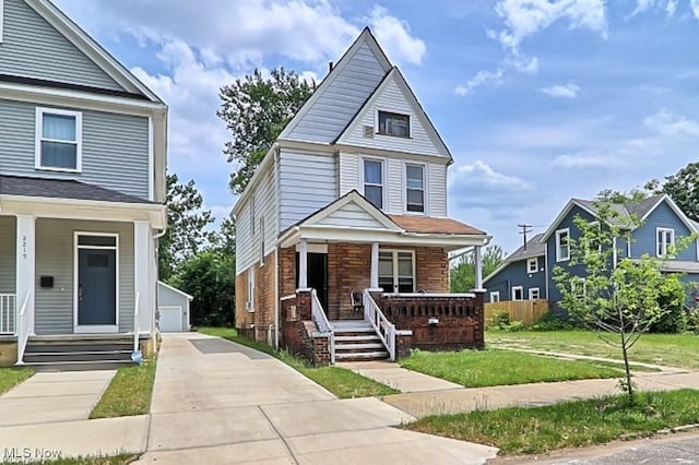 view of front of home with brick siding, a detached garage, an outbuilding, covered porch, and a front yard