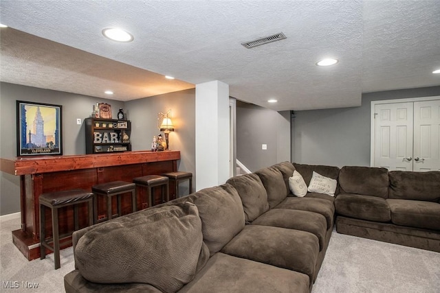 carpeted living area with a textured ceiling, recessed lighting, visible vents, baseboards, and a dry bar