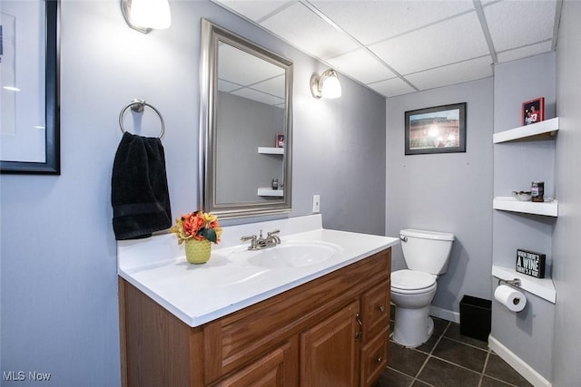 bathroom featuring a drop ceiling, toilet, vanity, baseboards, and tile patterned floors