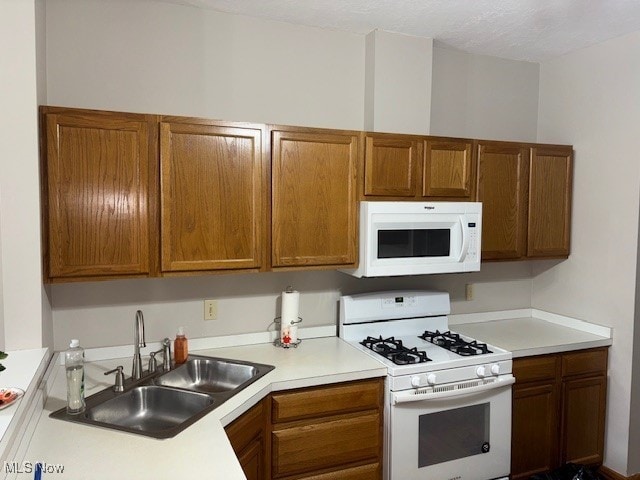 kitchen with light countertops, white appliances, a sink, and brown cabinets