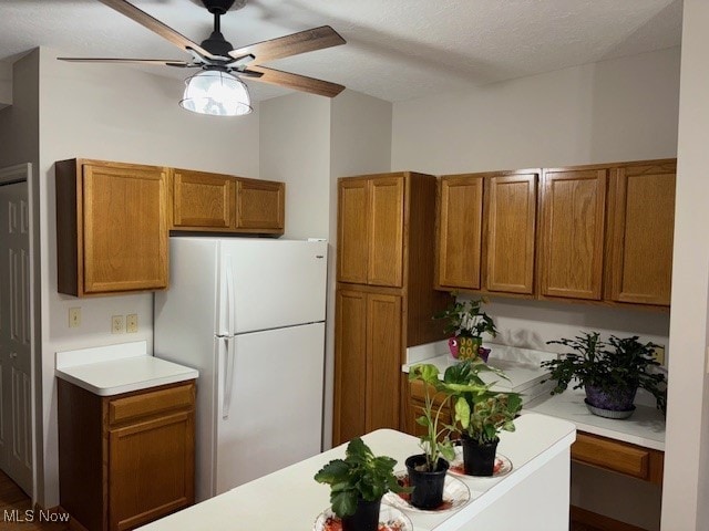 kitchen with brown cabinetry, light countertops, a ceiling fan, and freestanding refrigerator