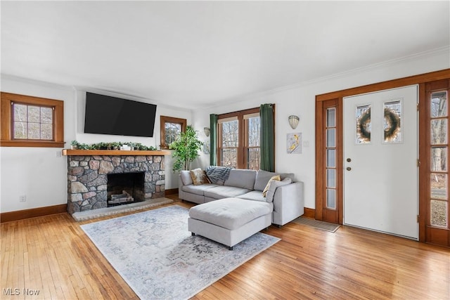 living area featuring ornamental molding, a stone fireplace, light wood-type flooring, and baseboards