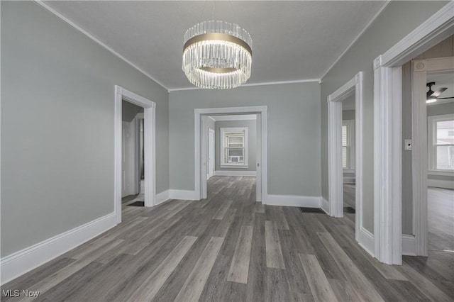 unfurnished dining area featuring baseboards, ornamental molding, wood finished floors, and an inviting chandelier