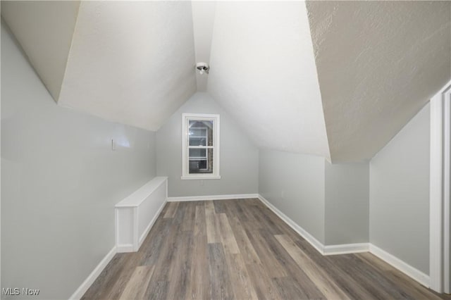 bonus room featuring a textured ceiling, baseboards, vaulted ceiling, and wood finished floors