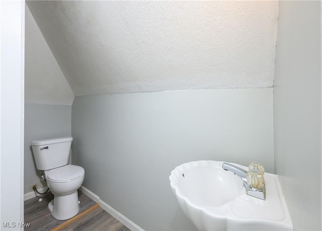 half bath featuring baseboards, toilet, lofted ceiling, wood finished floors, and a textured ceiling