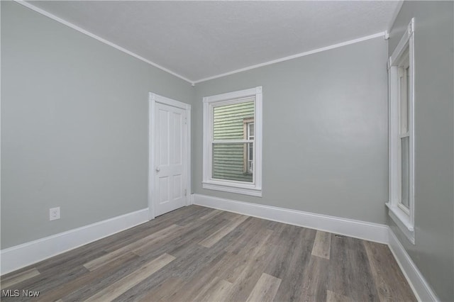 empty room with a textured ceiling, ornamental molding, wood finished floors, and baseboards