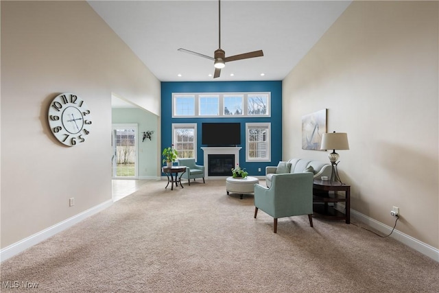 carpeted living area with a towering ceiling, ceiling fan, baseboards, and a glass covered fireplace