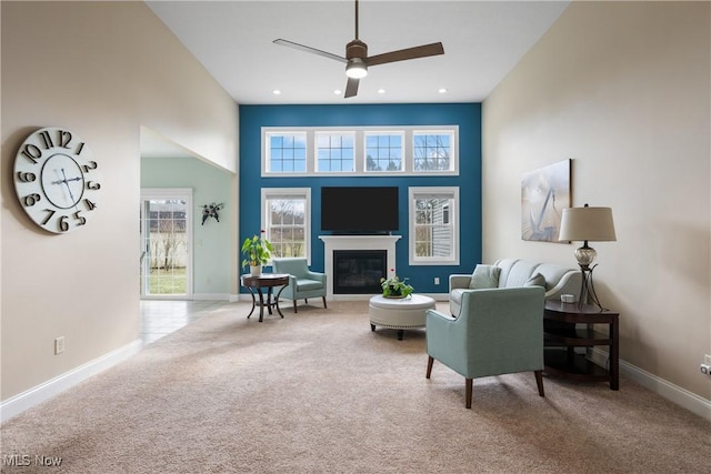 living area with a towering ceiling, baseboards, a glass covered fireplace, and light colored carpet