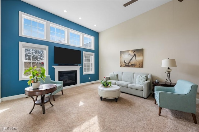 living room featuring recessed lighting, light colored carpet, a towering ceiling, baseboards, and a glass covered fireplace